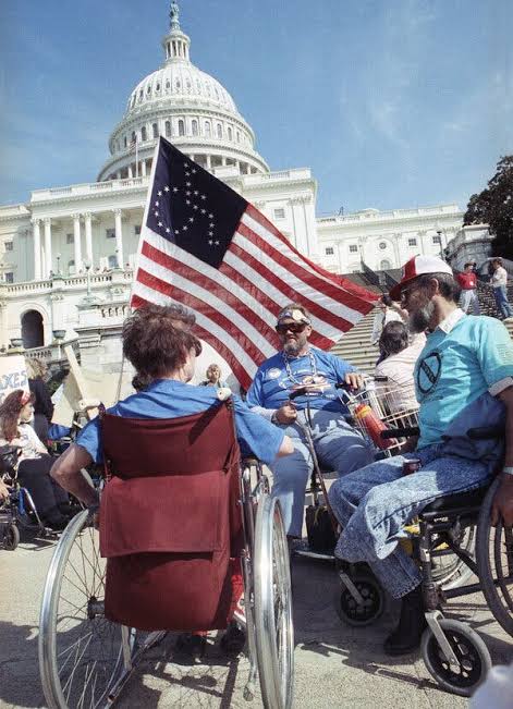 Disability rights activists in wheelchairs with an American flag in front of the U.S. Capitol